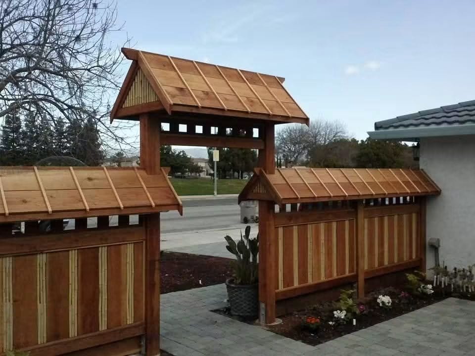Wood gateway and fence with small peaked roofs and bamboo accents