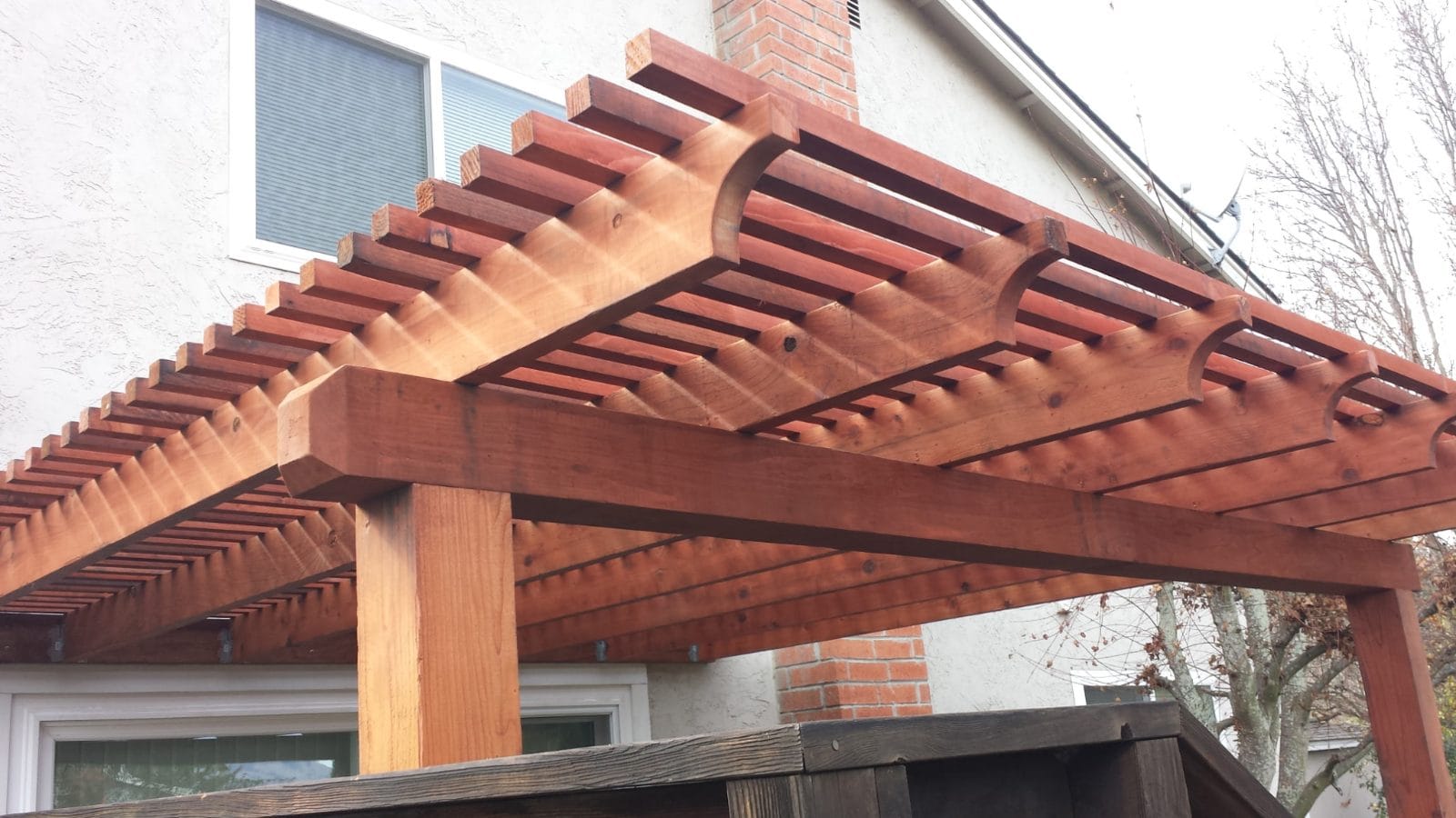 Wood pergola with shaped rafter ends beside a house